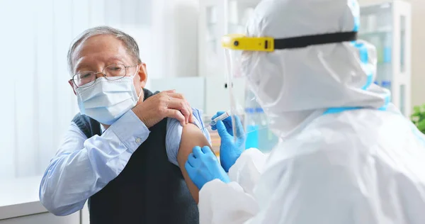 asian female nurse wearing gloves and isolation gown is making a COVID19 vaccination in the shoulder of senior male patient at hospital