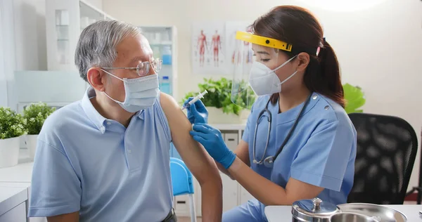 亚洲女护士戴着手套和隔离面罩 在医院的老年男病人肩部接种了Covid 19疫苗 — 图库照片