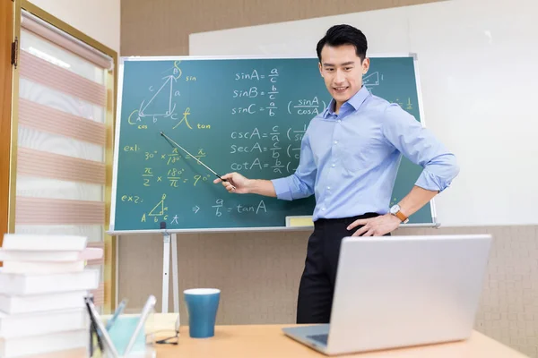 asian senior high school male teacher teach math online through laptop in classroom