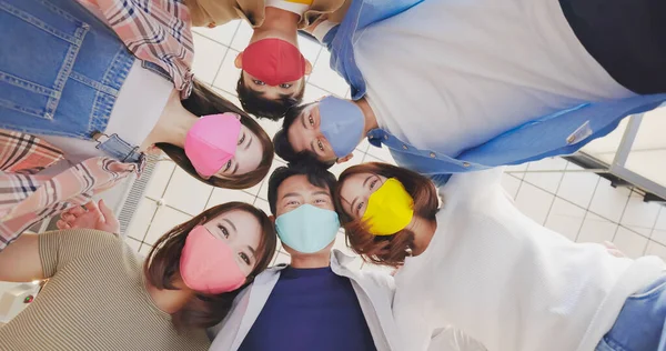 Directly below shot of asian young friends wearing colorful face mask are hugging and their head forming a circle indoor