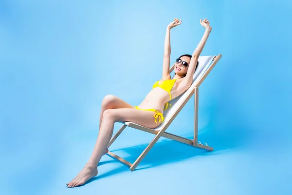 夏日防晒霜和旅游理念 亚洲比基尼女孩躺在海滩椅子上享受阳光孤零零的蓝色背景 — 图库照片