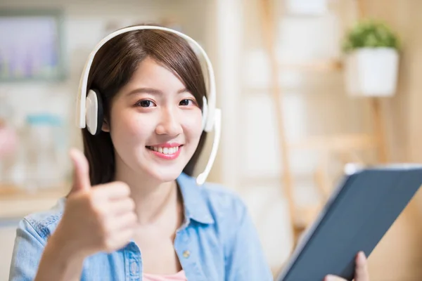 亚洲女人戴着耳机对着你微笑 在家里举着带着大拇指的数码平板电脑 — 图库照片