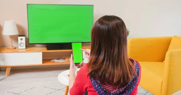亚洲的年轻女子一个人在家里的沙发上使用智能手机和绿色彩色电视 — 图库照片