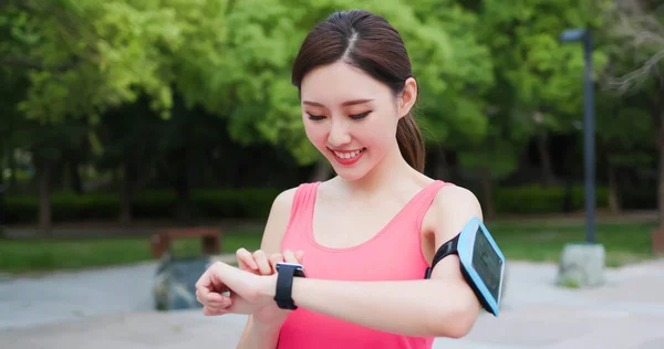 スポーツアジアの女性はスマートウォッチを着用して公園内のスマートフォンで走ります — ストック写真