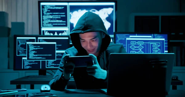 closeup of asian male hacker using cellphone to steal mobile game with computer