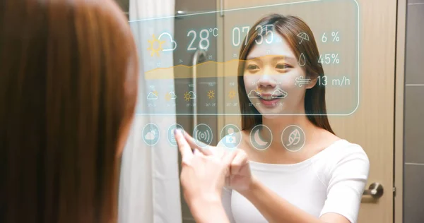 亚洲女人醒来后在浴室里看着并触摸着智能屏幕 在镜子前提供天气信息 — 图库照片