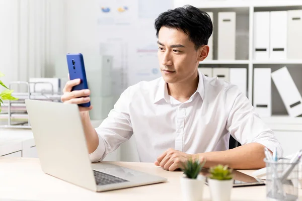 Aasialainen Nuori Liikemies Käyttää Älypuhelinta Tietokonetta Toimistossa — kuvapankkivalokuva