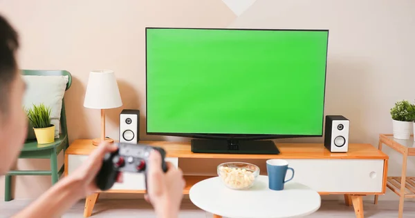 坐在沙发上 手里拿着无线控制器 在家里一个绿色彩色键电视屏幕上玩电子游戏的亚洲年轻游戏男孩的近照 — 图库照片