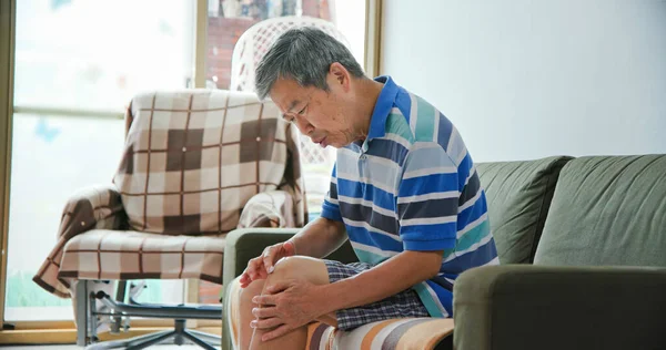 asian elder man has joint pain and he is applying ointment cream on his knees at home