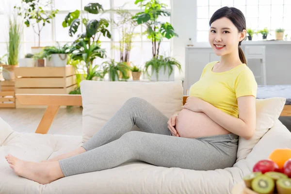 アジアの妊婦はソファに横たわって幸せと彼女の腹に触れる — ストック写真