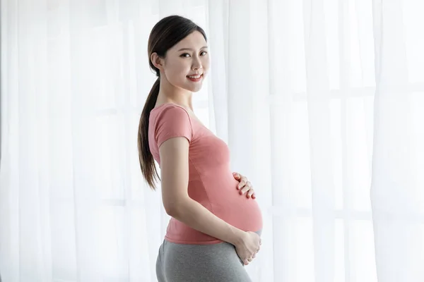 아름다운 아시아인 임산부가 창가에 거실에서 미소짓고 — 스톡 사진