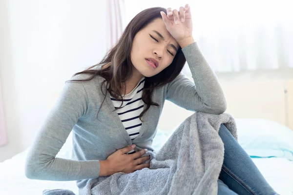 亚洲女性病人坐在床上头疼 肚子痛 — 图库照片