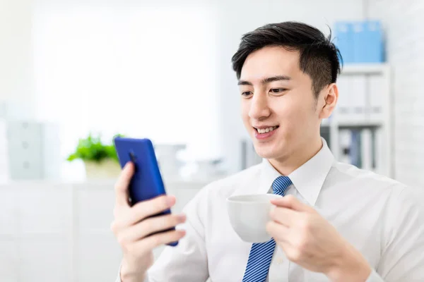 아시아 사업가가 스마트폰으로 뉴스를 사무실에서 커피를 마시고 있습니다 — 스톡 사진