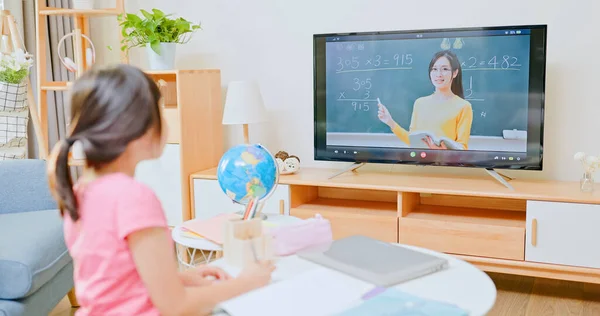 亚洲女孩的后视镜是在客厅里学习数学和在电视上看在线课程 小学女教师 而地方当局则宣布呆在家里 — 图库照片