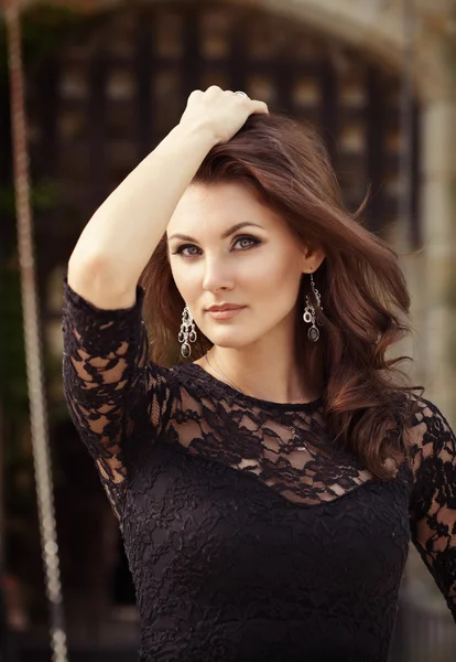 Portrait of elegant lady in little black lace dress standing on the castle background touching her beautiful brunette hair — Stock Photo, Image