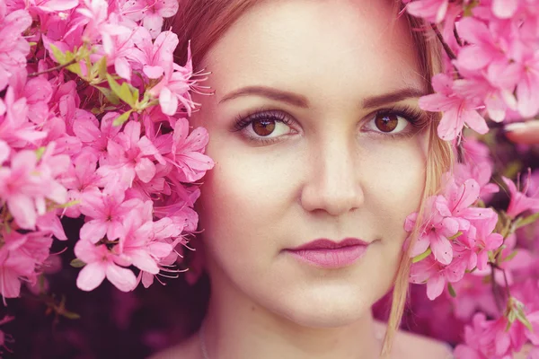 Portré fiatal kaukázusi nő körül a rózsaszín tavaszi virágok — Stock Fotó