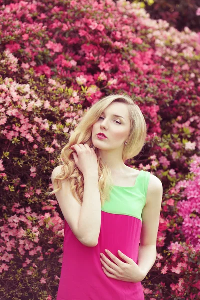 Jonge blonde model poseren voor roze voorjaar bloemen achtergrond — Stockfoto