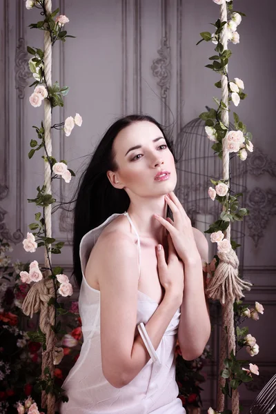 Krásná bruneta se zhluboka dýchat, sedí na květinové houpačky a drží ruce u krku Stock Obrázky
