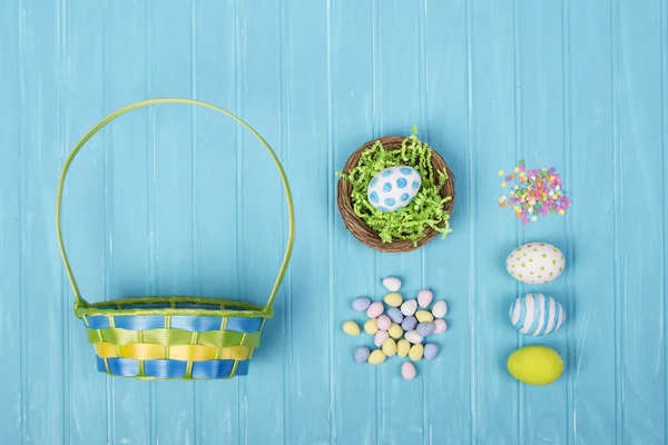 Великодні яйця, кошик і цукерки на синьому фоні — стокове фото