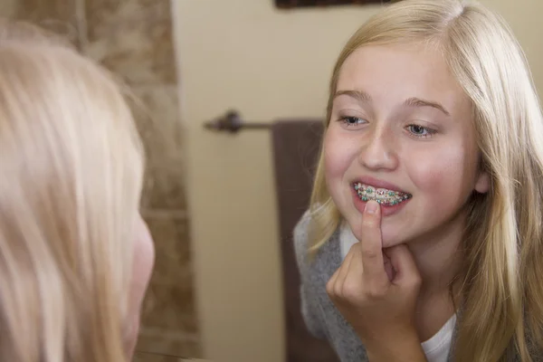 Ragazza che si guarda allo specchio, esaminando il suo apparecchio — Foto Stock