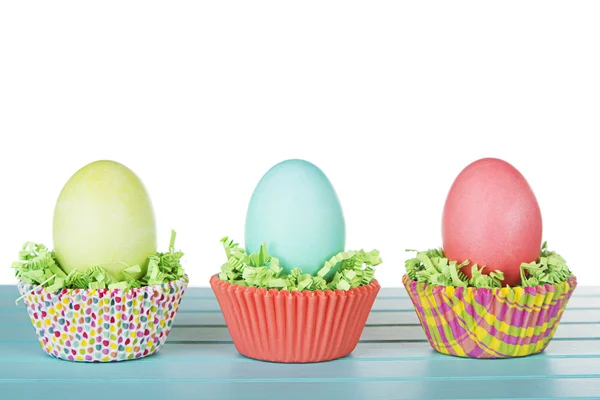 Dyed Easter eggs in a nest of green grass confetti and cup cake — Stock Photo, Image