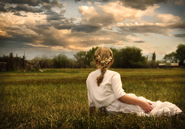 Girl wearing a dress sitting in a pasture — Stock Photo, Image