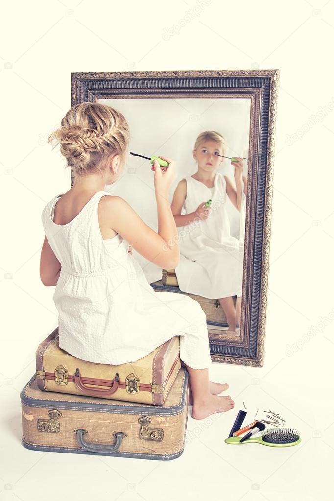Child or young girl putting on make-up while looking at herself 