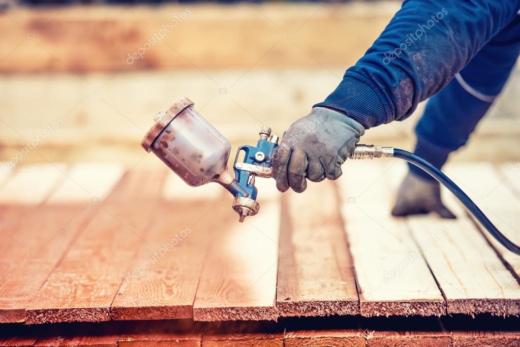Man using protective gloves painting wooden timber with spray paint gun