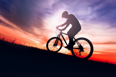 Sunse gökyüzü arka plan ile bisiklet üzerinde bir bisikletçinin silüeti