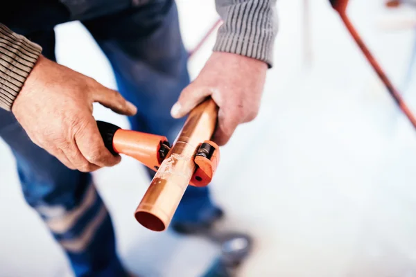 Encanador industrial cortando um tubo de cobre com um cortador de tubos — Fotografia de Stock