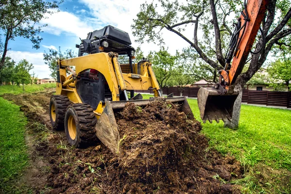 Gul mini bulldozer arbetar med jorden, flyttar jord och gör landskapsplanering fungerar — Stockfoto