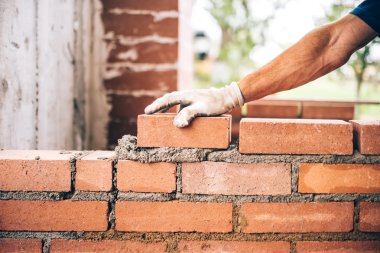Endüstriyel tuğla ustası dış duvarlar inşa ederken çimentoya tuğla yerleştiriyor, endüstri ayrıntıları
