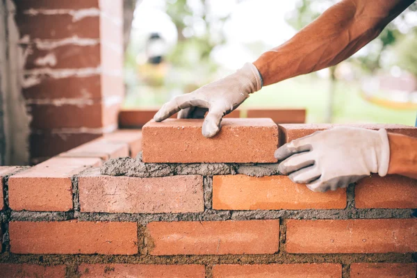 Trabalhador da construção civil profissional que coloca tijolos e churrasqueira construção em local industrial. Detalhe da mão ajustando tijolos — Fotografia de Stock