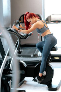 Spor salonunda staj bisikleti kullanan, spor yapan aktif bir kadın.