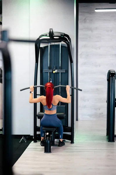 근육질의 여자가 체육관에서 근육에 펌프질을 시뮬레이터를 사용하고 있습니다 — 스톡 사진