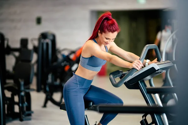 Fit active woman in the gym, working out and smiling on stationary bicycle at gym.  Fitness and bodybuilding concept