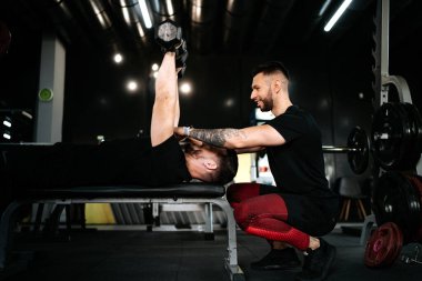 Gülümseyen adam, kişisel antrenör spor salonunda müşteriye yardım ediyor ve göğüs egzersizi yapıyor. Kişisel antrenörle sağlıklı yaşam tarzı fitness oturumu