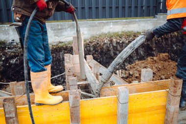 İnşaat işçisi inşaat alanında çimento sallıyor. Beton vibratör kullanan işçiler ve otomatik pompa kullanan ve çimento yöneten diğer işçiler 