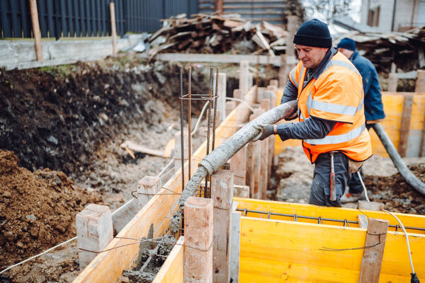 caucasian workers pouring concrete with concrete pump and hose. Details of construction site and close up details of worker workwear