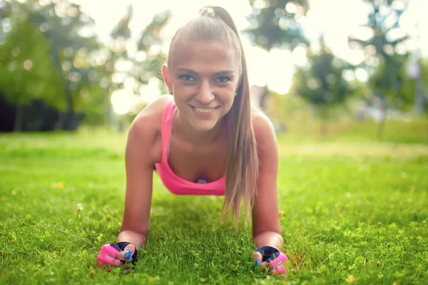 Glad, vacker blond tjej gör abs och isometrier på gräset i parken — Stockfoto