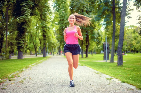 Donna sana e felice che corre nel parco urbano con cuffie e musica — Foto Stock