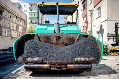 Industrial paver laying fresh asphalt and bitumen pavement on top of gravel layer during road construction