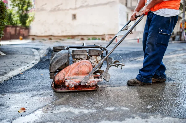 Asfaltarbeider ved reparasjon av vei med manuell komprimeringsplate – stockfoto