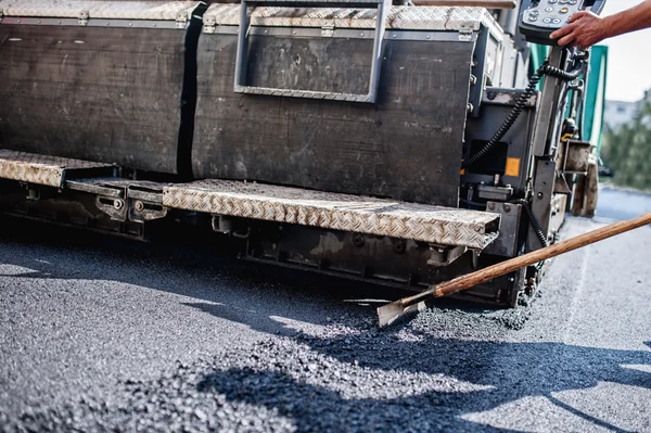 Trabajador masculino operando maquinaria de pavimentadora de asfalto en el sitio de construcción de carreteras y trabajos de reparación — Foto de Stock