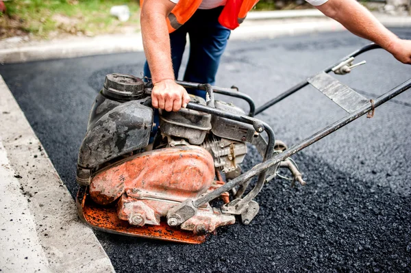 Trabajador de asfalto en obra viaria con placa compactadora y herramientas — Foto de Stock