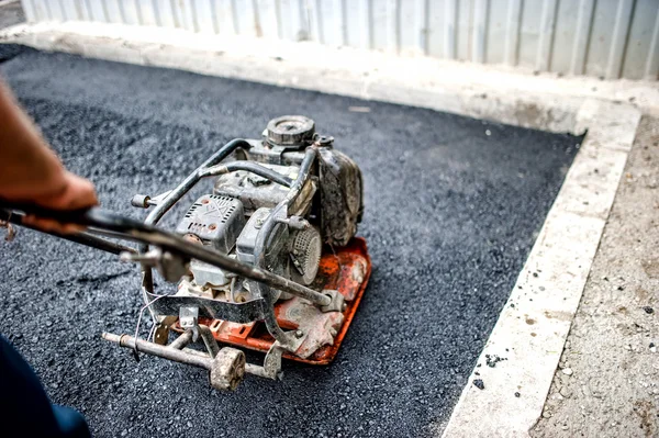 Close-up of asphalt worker in construction site with manual compactor plate — Stock Photo, Image