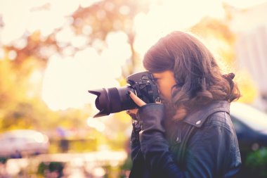 Attractive young woman photographer taking pictures with professional digital camera outside. vintage effect clipart