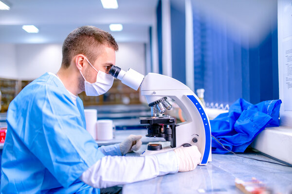 Scientist working in chemistry laboratory, examining samples at microscope