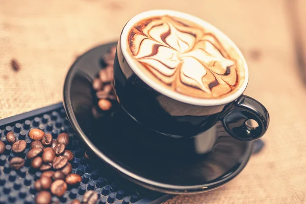 Tazza nera di caffè esspresso appena preparato. Primo piano della tazza di caffè con latte e fagioli. Effetto morbido . — Foto Stock