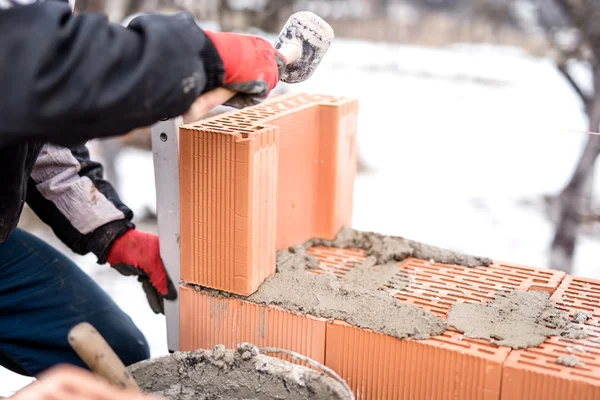 Hombre en el sitio de construcción trabajando con ladrillos y mortero, la construcción de paredes de la casa en invierno — Foto de Stock